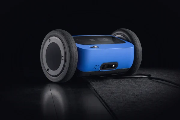 A small wheeled robot base with one wheel on a smooth tile and the other on a scuffed mat with a cable across it